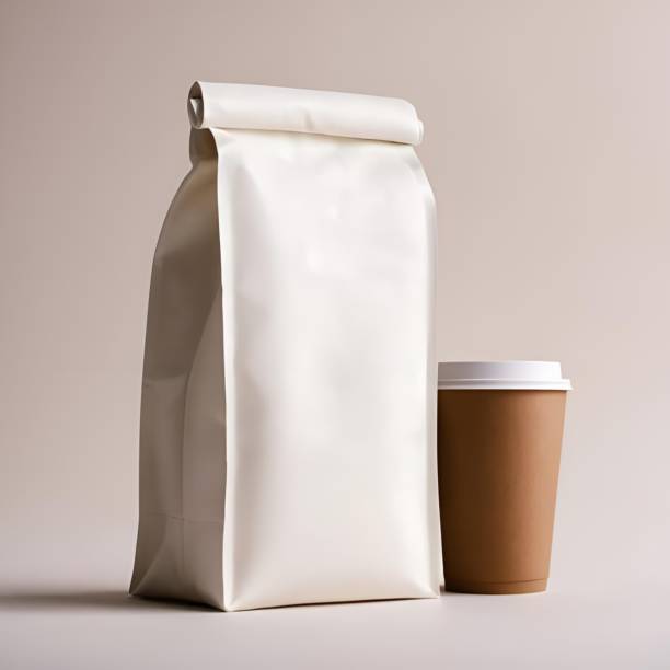 The image captures a moment of morning tranquility, featuring a pristine white coffee bag alongside a brown takeaway coffee cup with a white lid. The coffee bag, unopened and full, suggests the promise of a fresh brew, while the cup awaits to be filled with a warm beverage. Set against a soft, neutral background, the scene evokes the serene start of a day, with the soft lighting adding to the calm and inviting atmosphere. Perfect for a quiet morning pause or the beginning of a busy day, these essentials speak to coffee lovers everywhere.