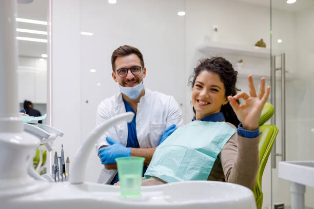 A smiling woman in dental chair gives an OK sign next to her male dentist in a modern clinic Both look at the camera and seem content