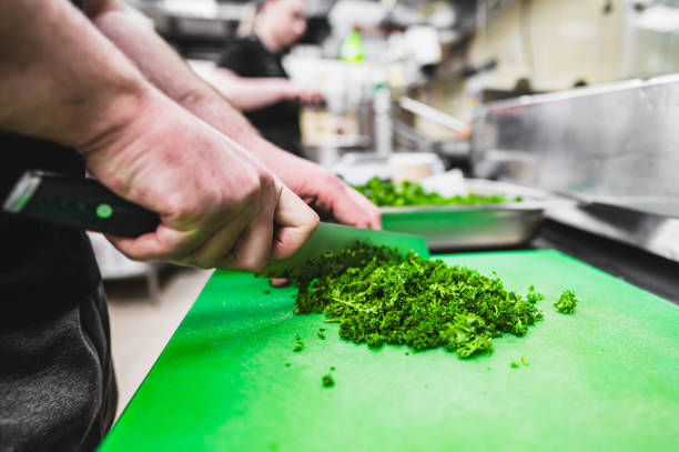 Close-up of hands chopping fresh green herbs on a cutting board in a kitchen setting