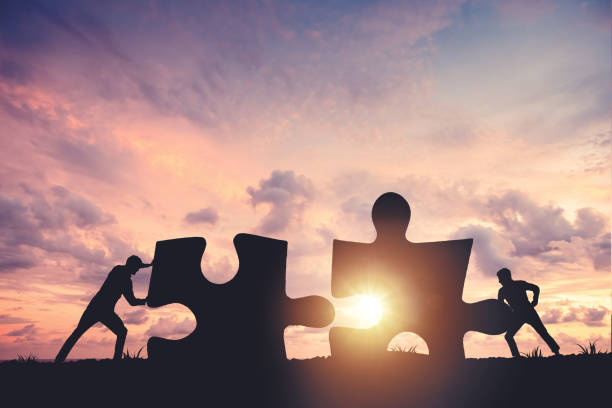 istock Silhouette of a team folding a puzzle against a sunset background, business and teamwork concept 2153879349