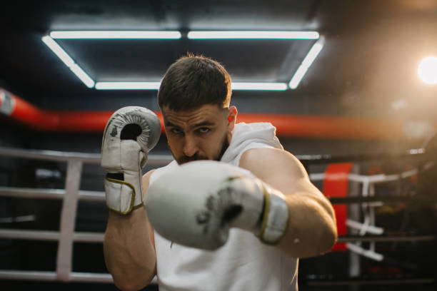 istock Strong young boxer training with boxing gloves in the gym. A determined young man practices his punching technique during training at a boxing club. 2153880621