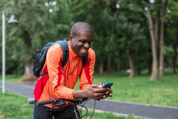istock Smiling man with bicycle using smart phone outdoors in park 2153880712