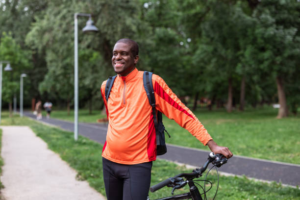 istock Man smiling while standing with his bicycle in a park 2153880758