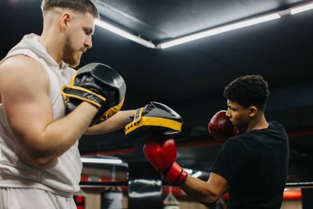 istock A male trainer helps a teenage boxer with striking techniques in a boxing ring. 2153881396