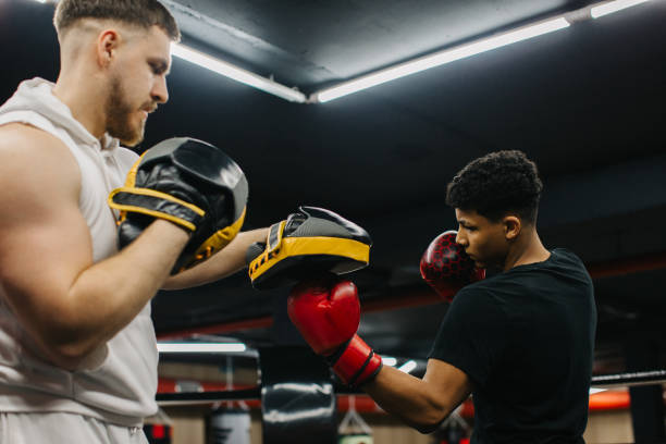 istock A male trainer helps a teenage boxer with striking techniques in a boxing ring. 2153881397