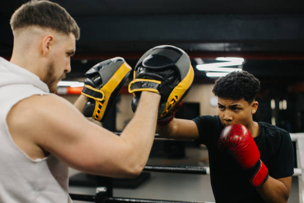 istock A male trainer helps a teenage boxer with striking techniques in a boxing ring. 2153881403