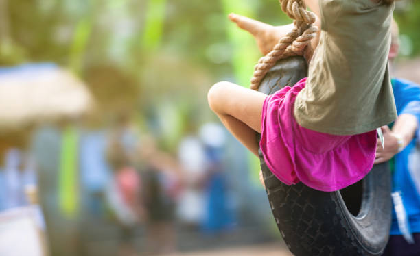 A barefoot girl in a skirt, sitting on a swing made of a car tire and swinging