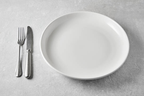 istock White ceramic plate with knife and fork on a gray stone table. Template for displaying food on the menu 2153891418
