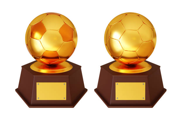 Two Golden Soccer Trophies Displayed on a Red Table at an Outdoor Field