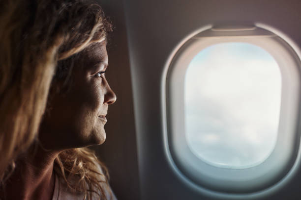 Profile view of smiling woman looking through window while traveling by airplane.
