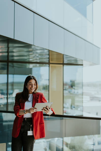 istock Smiling businesswoman in red blazer using tablet at modern office window in daylight 2153929967