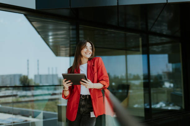 istock Smiling businesswoman in red blazer using tablet at modern office window in daylight 2153929972