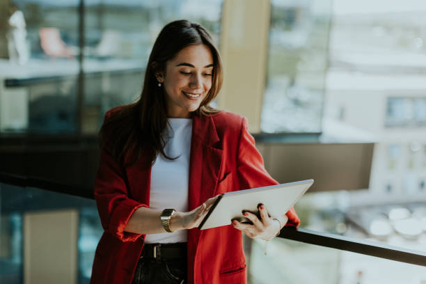 istock Smiling businesswoman in red blazer using tablet at modern office window in daylight 2153929981