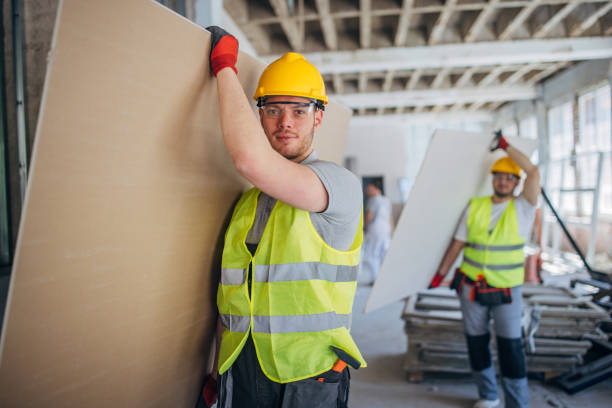 istock Two construction workers in safety gear efficiently transport drywall sheets at a construction site 2153932127