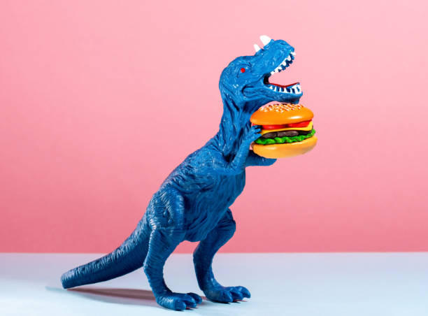 istock Close up blue dinosaur holding burger on pink and blue background. 2153932353
