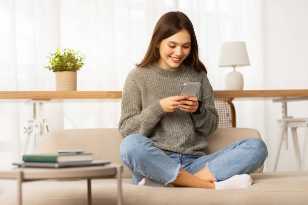 istock Cheerful young woman student sitting on couch, using smartphone 2153933264