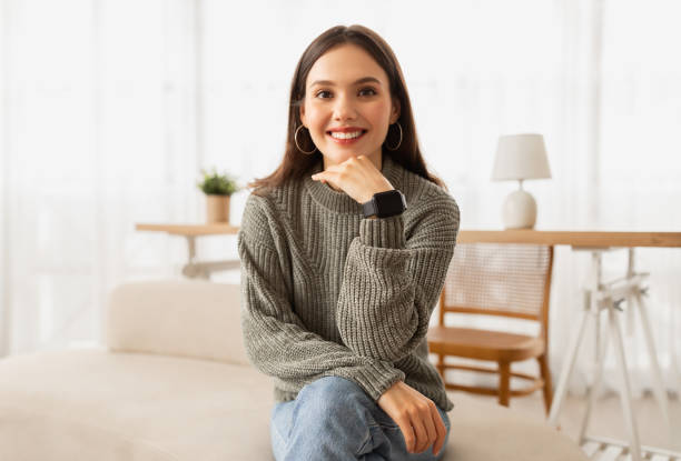 istock Attractive woman sitting on couch at home, smiling at camera 2153933298