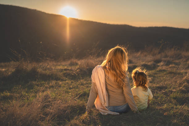 istock Mother and daughter looking at sunset on the hill 2153936028