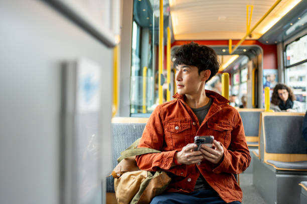 Backpacker traveler man using mobile phone while riding on the train. Attractive male tourist swiping on smartphone, travel alone with modern transportation enjoy holiday vacation trip in Switzerland.