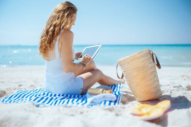 istock relaxed woman on ocean shore using applications on tablet PC 2153939482