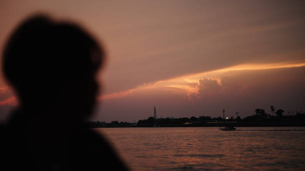 In silhouette of man solo traveling at local riverside during sunset.