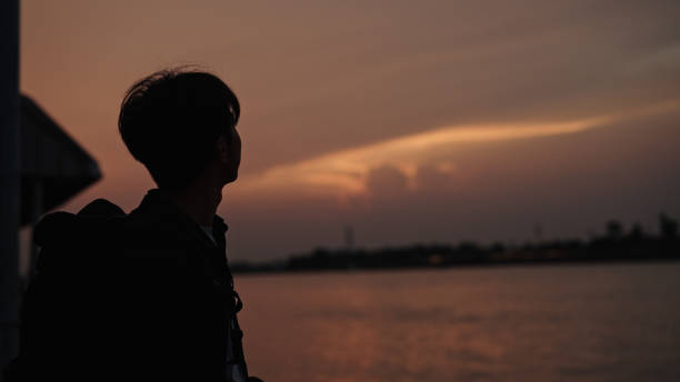 In silhouette of man solo traveling at local riverside during sunset.