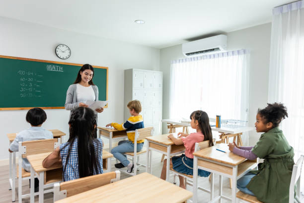 Group of student learn with teacher in classroom at elementary school. Attractive beautiful female instructor master explain and educate young children with happiness and fun activity at kindergarten.