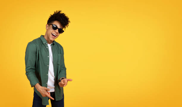 istock Stylish african american guy wearing sunglasses gesturing on yellow 2153942230