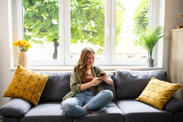 istock Young Caucasian woman sitting on the sofa and using mobile phone 2153945925