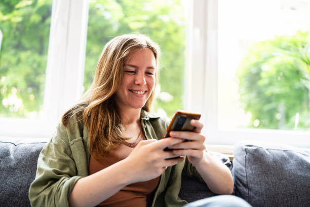 istock Young Caucasian woman sitting on the sofa and using mobile phone 2153945951
