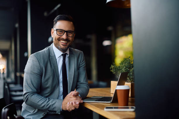 istock Happy businessman using laptop in a cafe and looking at camera. 2153946558