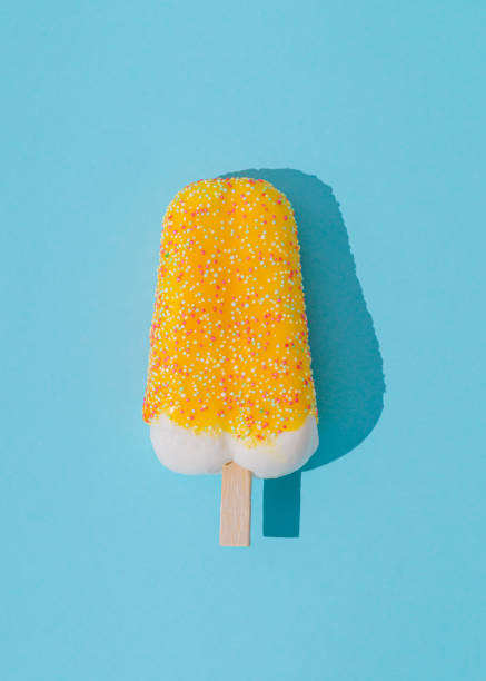 Yellow ice cream popsicle on light aqua blue background. Minimal summer concept. Ice cream aesthetic. Flat lay.