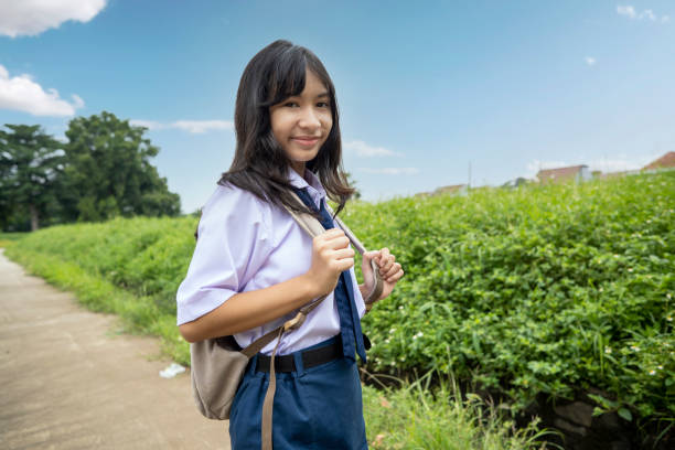 Young female Indonesian with junior hich school uniform wearing backpack going to school by walking against green scenery as background