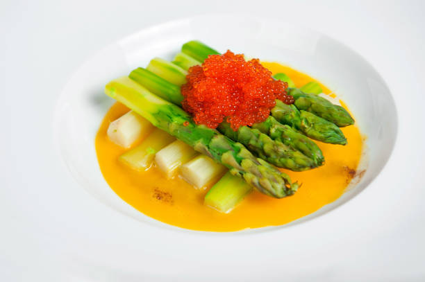 Elegant dish of green asparagus topped with red caviar, served on a sleek white plate