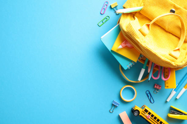 istock Back to School Flat Lay. A yellow backpack spills vibrant school supplies on a blue backdrop. Ideal for education and stationery themes 2153957292