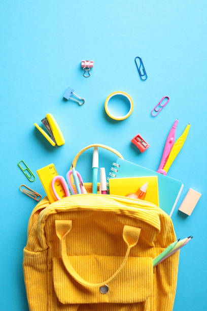 istock Yellow backpack filled with colorful school supplies on a bright blue background. Back to school concept. 2153958421