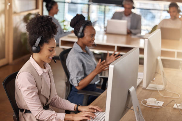 istock Call center, team and computer on desk in office for customer service, sales or support. Happy people, agents or consultant in night telemarketing, telecom and crm or help desk in coworking workplace 2153959411