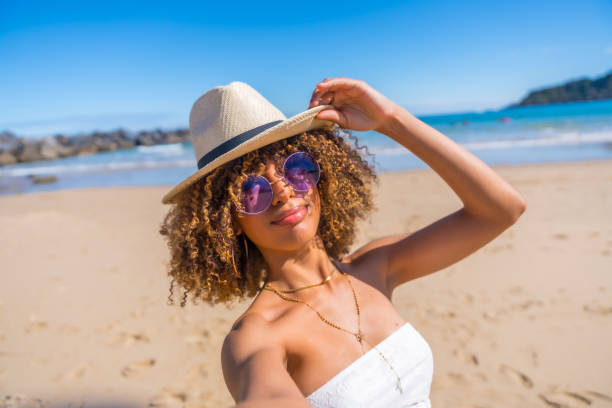 istock Latin woman holding a sun hat taking selfie a beach 2153960248
