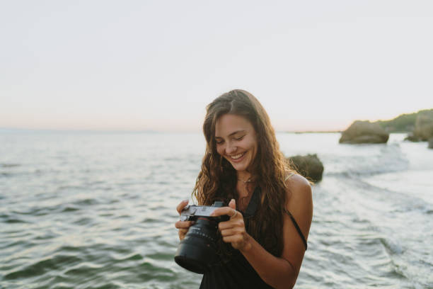 Photo of a young woman holding a digital camera, photographing, as she is vacationing on the beach by the sea