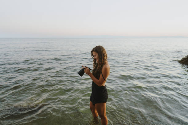 Photo of a young woman holding a digital camera, photographing, as she is vacationing on the beach by the sea