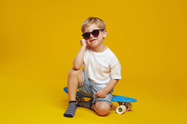 istock Handsome kid in sunglasses smiling and supporting head while sitting on blue modern skateboard. 2153965401