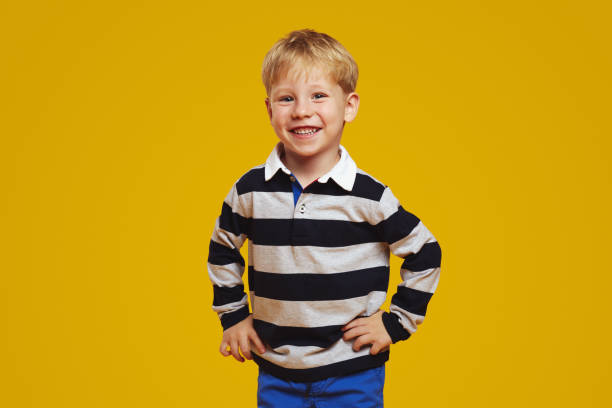 istock Joyful kid wearing striped shirt and keeping hands on waist while smiling brightly at camera. 2153965747