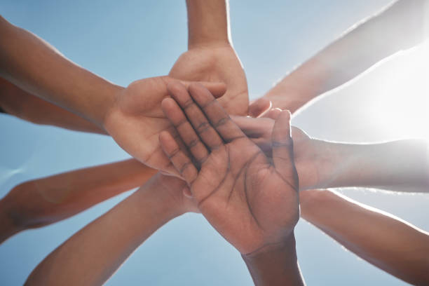 Hands, team and community below in support, trust or collaboration against a blue sky background. Group hand of people together in teamwork, meeting or partnership for unity, agreement or motivation
