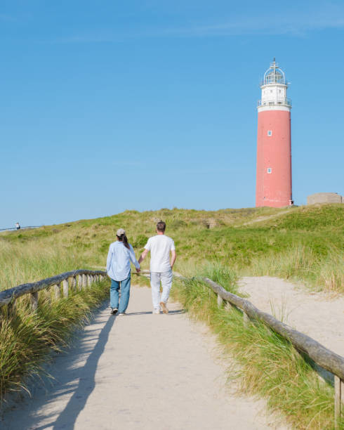 istock Two individuals strolling along a path near a charming lighthouse in Texel, Netherlands, enjoying the serene coastal scenery 2153967921