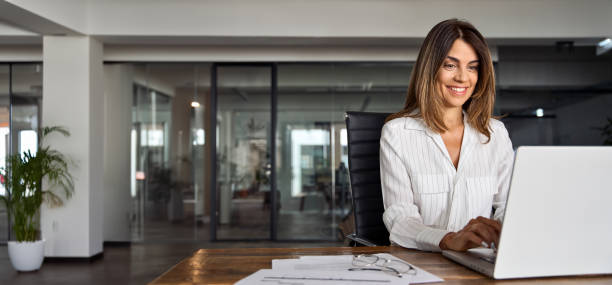 istock Mature Latin businesswoman using computer, typing, working in modern office. Ceo woman doing online business data market analysis, thinking planning tech strategy looking at laptop, copy space. Banner 2153986423