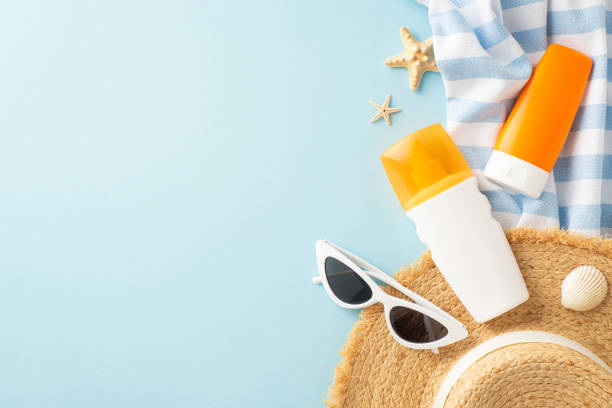 istock A creatively arranged beach scene featuring sunscreen bottles, a straw hat, sunglasses, and sea shells on a stripy towel against a light blue background 2153989008