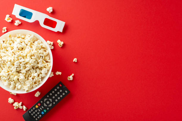 istock Indoor movie fest with delectable snacks. Top view vertical image showcasing popcorn, 3D glasses, remote. Vibrant red background, ideal for text or promotional content 2153989035