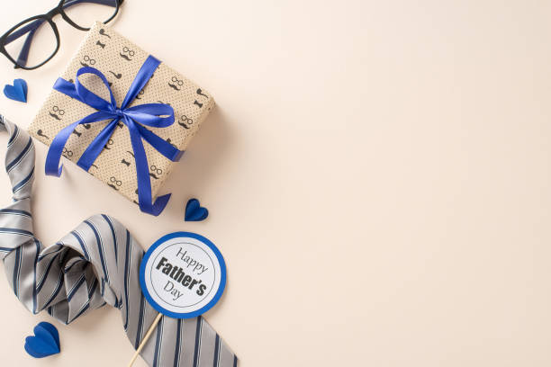 istock Celebrate Dad with a special Father's Day tribute using this design. A top view showcases a dapper tie, giftbox, glasses, postcard, paper hearts on a beige background, perfect for your heartfelt words 2153989062