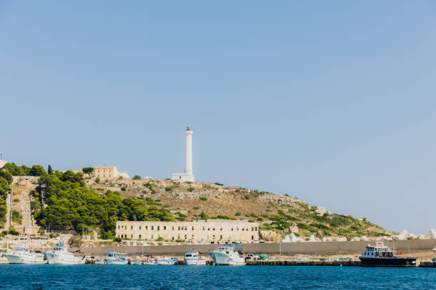 Sailing by rocky coastline with majestic while lighthouse in St Maria di Luca in Puglia, Italy