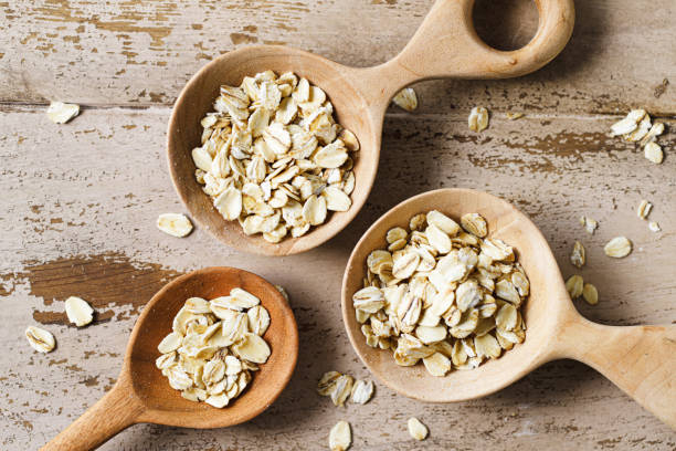 Top view of of oats in spoons on a wooden table. Organic rolled flakes for preparing oat milk.